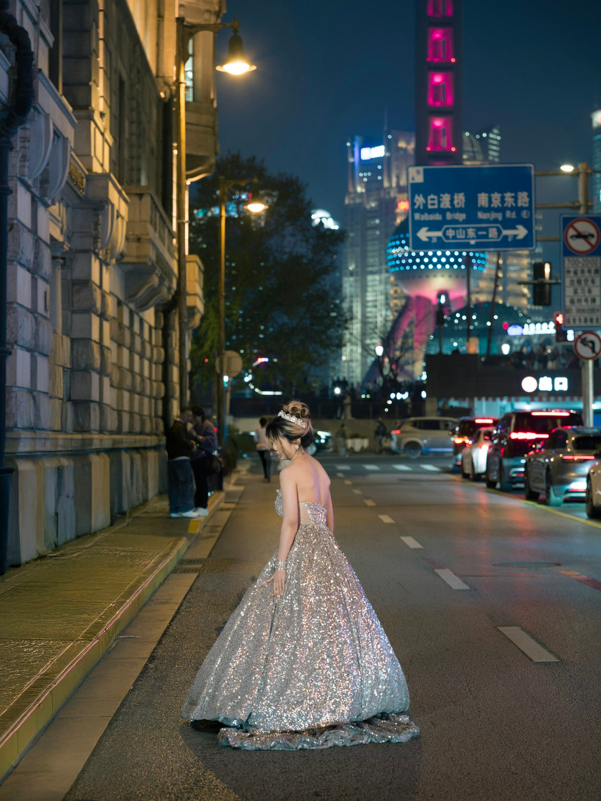 Woman in a sequined gown mid-stride on a city street at night, skyline lit behind her