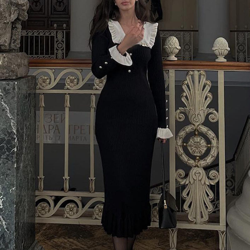 Woman in a black dress with white ruffled collar standing in an ornate interior setting.